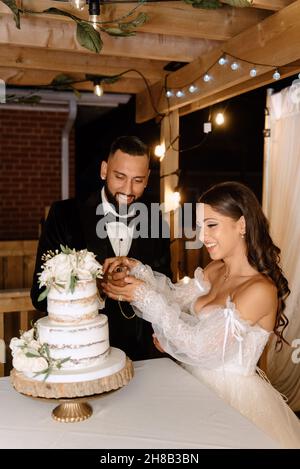 Sorridente sposa e sposo taglio torta di nozze Foto Stock
