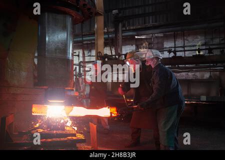 I lavoratori di Forge preformano la billetta di acciaio caldo rossa Foto Stock