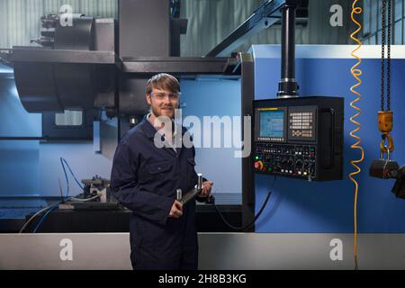 Apprendista tenendo un bullone a u reggetta nella parte anteriore della macchina CNC Foto Stock