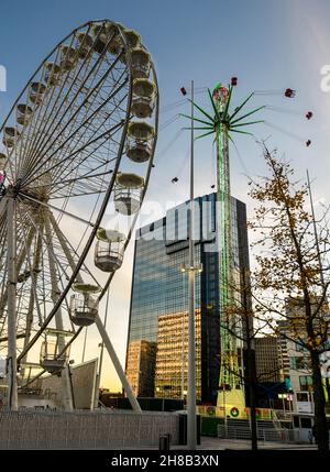 Giri su una ruota grande e sul terreno fieristico vicino a Natale nel soleggiato pomeriggio d'inverno, con cielo blu ed edifici moderni, accanto alla nuova Biblioteca di Birmingham. Foto Stock