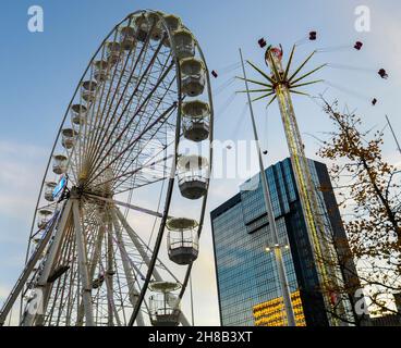 Giri su una ruota grande e sul terreno fieristico vicino a Natale nel soleggiato pomeriggio d'inverno, con cielo blu ed edifici moderni, accanto alla nuova Biblioteca di Birmingham. Foto Stock