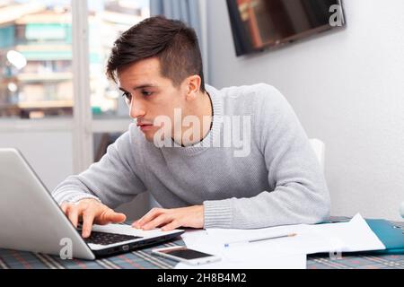 Sconvolto giovane uomo conta budget familiare su laptop Foto Stock