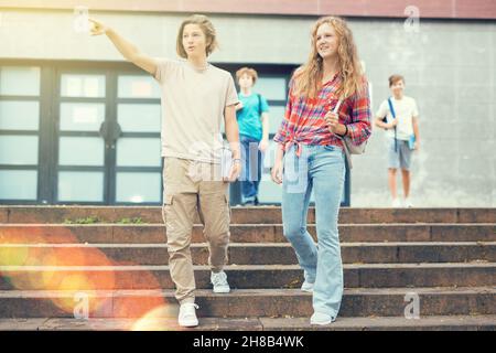 Gli studenti escono dalle porte dell'università. Il ragazzo punta la mano a qualcuno Foto Stock