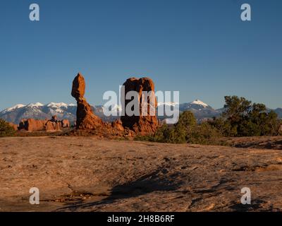 Formazione di arenaria rossa bilanciata di roccia in luce dorata con le montagne la SAL innevate sullo sfondo. Al Parco Nazionale Arches nello Utah Foto Stock