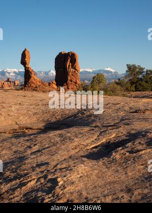 Vista ad angolo basso della formazione di pietra arenaria rossa bilanciata della roccia in luce dorata con le montagne la SAL innevate sullo sfondo. A Arches National Pa Foto Stock