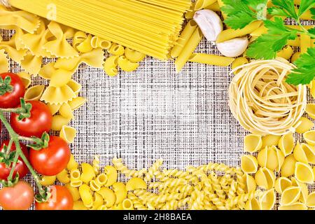 Cornice fatta di pasta, pomodori, aglio e prezzemolo diversi sullo sfondo di un tessuto grossolano di vimini Foto Stock