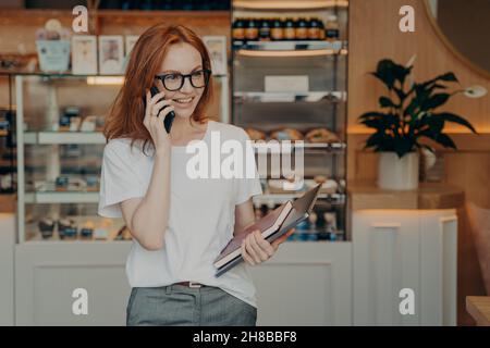 Sorridendo la giovane donna rossa ha conversazione telefonica gode di un colloquio positivo Foto Stock