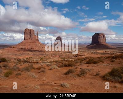 Monument Valley's West Mitten, East Mitten e Merrick Buttes con sabbia arancione in primo piano e cielo nuvoloso sopra. Foto Stock