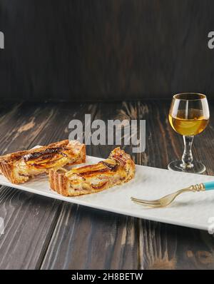 Torta di mele con fette di vaniglia affettate con un bicchiere di liquore, su sfondo di legno. Cucina gourmet francese Foto Stock