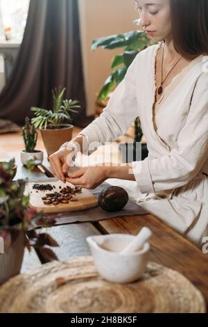 Donna mani peeling cacao biologico fagioli su tavola di legno, cacao pennini, cioccolato artigianale in stile rustico per la cerimonia sul tavolo. Degostazione Foto Stock