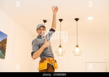 Giovani elettricista installazione rilevatore di fumo sul soffitto Foto Stock