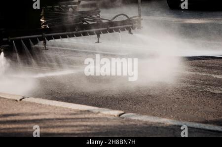 Pulendo lavatrici lavatrici lavatrici la strada delle strade della città con acqua nebulizzata, gruppo di annaffiatrici comunali lavano asfalto, Foto Stock