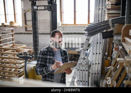 Carpentiere maschio maturo che fa l'inventario all'interno in officina di carpenteria. Concetto di piccola impresa. Foto Stock