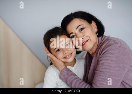 Piccola ragazza felice con nonna anziana in casa guardando la macchina fotografica. Foto Stock