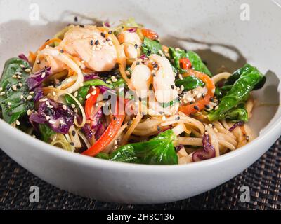 wok cinese, mescolare noodle di riso fritto con gamberi, peperone e spinaci in salsa di soia, servito in una ciotola su sfondo scuro, foto orizzontale Foto Stock