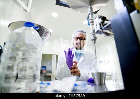 Giovane chimico che mette i suoi guanti di preparazione per il lavoro. Camera sterile nel laboratorio di produzione dell'acqua. Foto Stock