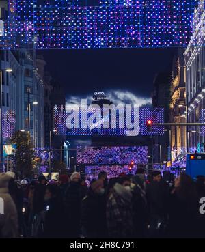 Madrid, Spagna - 28 novembre 2021: Decine di persone attraversano la strada sotto le luci di Natale in Gran Via, Madrid, Spagna. Foto Stock