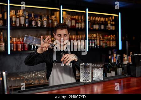Barman in grembiule aggiunge l'ingrediente al vetro Foto Stock