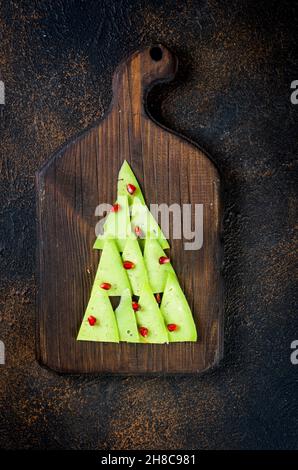 Pezzi di formaggio assortiti e frutta disposti in forma di albero di Natale su tavola scura, decorazione di festa tavolo, Foto Stock