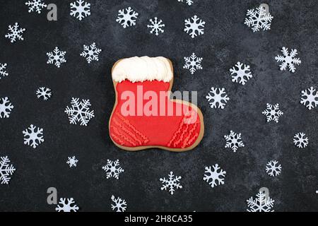 Gustosi biscotti di pan di zenzero a forma di scarpone e fiocchi di neve su sfondo scuro. Scorte di Capodanno. Pasticceria di festa. Dolci invernali tradizionali. Disposizione piatta, vista dall'alto. Stagione invernale Foto Stock
