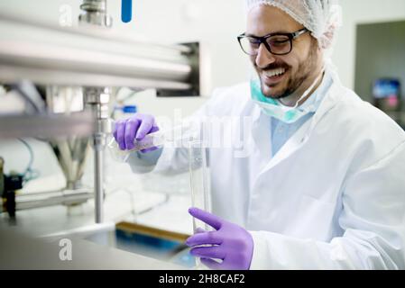 Tecnico di laboratorio sorridente che esegue l'analisi dell'acqua, vestito con un'apparecchiatura sterile protettiva. Foto Stock