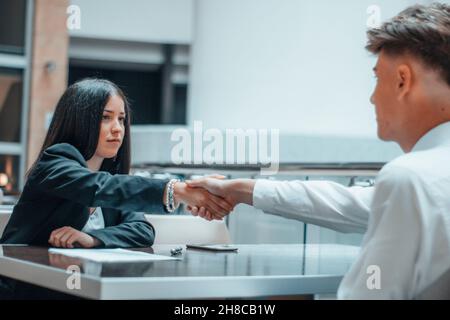 La giovane ragazza esegue una stretta di mano al tavolo con il suo cliente nel suo ufficio Foto Stock