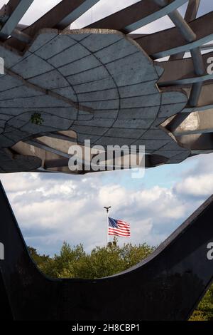 Una vista insolita di una bandiera americana che soffia nel vento come visto attraverso la base dell'Unisphere in Flushing Meadows Corona Park, Queens, New York. Foto Stock