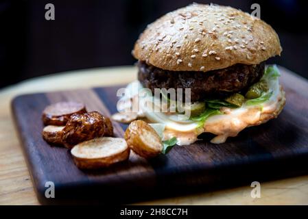 Delizioso cheeseburger con panino croccante su un asse di legno Foto Stock