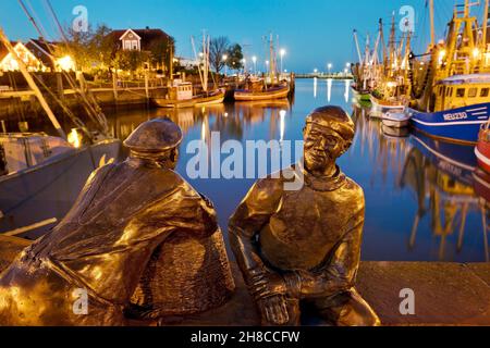 Porto di pesca con gamberetti e sculture skulptur Alt- und Jungfischer in serata, Germania, bassa Sassonia, Neuharlingersiel Foto Stock