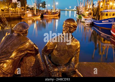 Porto di pesca con gamberetti e sculture skulptur Alt- und Jungfischer in serata, Germania, bassa Sassonia, Neuharlingersiel Foto Stock