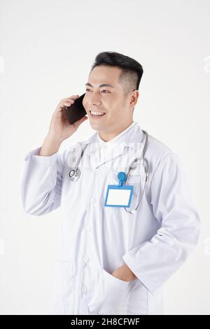 Ritratto di medico positivo in camice bianco mettere mano in tasca e parlare al telefono con il paziente Foto Stock
