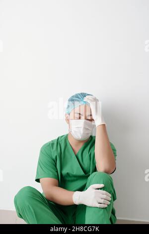 Stressato chirurgo esausto seduto sul pavimento con gli occhi chiusi dopo aver allentato il paziente Foto Stock