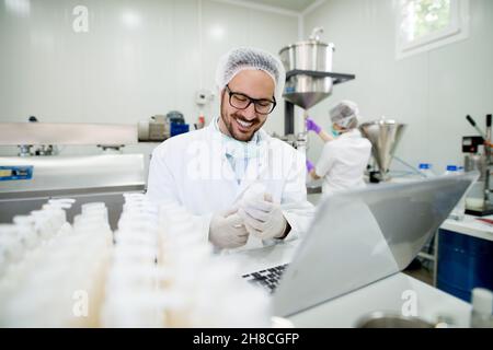 Giovane tecnologo sorridente che testa creme per la cura del viso. Seduto in una fabbrica di prodotti cosmetici. Foto Stock