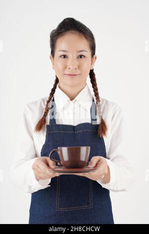 Ritratto di cameriera giovane e positiva che serve una tazza di gustoso caffè al cliente in coffee shop Foto Stock