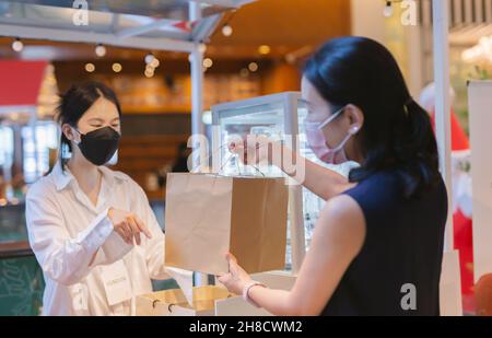 Sociale distanza concettuale donna proprietario in maschera protettiva dando cibo sacchetto al cliente. Foto Stock