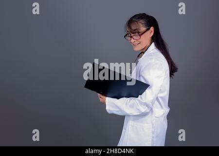 medico caucasico femminile nei suoi 40s con i capelli lunghi cartella in mano, lato di fronte alla macchina fotografica. Foto Stock