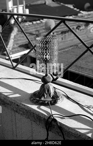 Scatto verticale in scala di grigi di una lampada sulla ringhiera di un tetto durante la luce del giorno Foto Stock