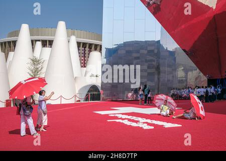 I visitatori hanno avuto ombrelloni rossi da posare all'esterno del Padiglione Svizzero, che era uno specchio gigante che riflette il tappeto rosso, Expo 2020, Dubai, Emirati Arabi Uniti Foto Stock