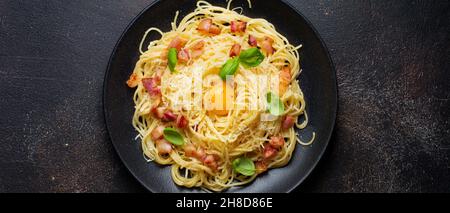 Pasta spaghetti carbonara con pancetta, parmigiano, tuorlo d'uovo e foglie di basilico su sfondo nero. Piatto tradizionale italiano. Vista dall'alto. Foto Stock