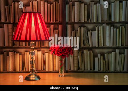 Lampada da tavolo con ombra rossa e un mazzo di rose rosse davanti ad un bookself Foto Stock