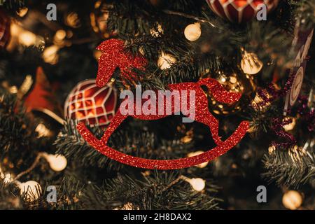 Giocattolo vintage sotto forma di un cavallo rosso lucido appeso sull'albero di Natale. Sfondo festivo. Dettagli fata di Capodanno Foto Stock