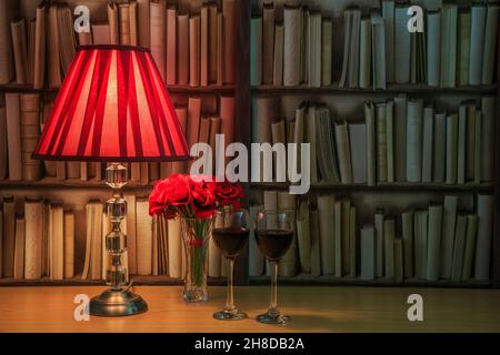 Lampada da tavolo con paralume rosso, due bicchieri pieni di vino rosso e un mazzo di rose rosse di fronte ad un libro Foto Stock