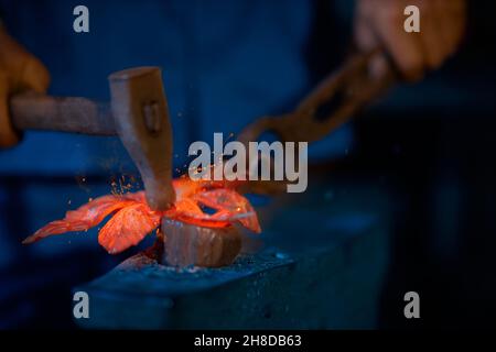 Primo piano l'uomo anziano in abito blu scuro che lavora con attrezzi speciali che fanno decorazioni per recinzione in moderno smithy. Concetto di lavoratore che fa decorazioni con fuoco in luogo speciale. Foto Stock