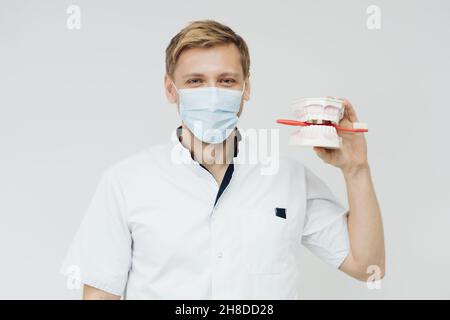 Dentista che mostra la corretta igiene dentale utilizzando mock-up di scheletro di denti. Medico stomatologo che spiega la corretta igiene dentale per il paziente che tiene un campione di mandibola umana con spazzolino da denti. Foto Stock