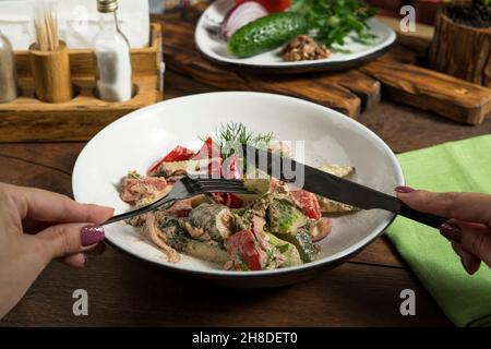 Insalata georgiana con verdure e noci in un piatto bianco. Mani femminili che tengono le posate Foto Stock