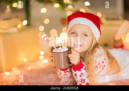 Bella ragazza caucasica di cinque anni che indossa pigiama di Natale quando si diverte a casa durante le vacanze invernali. Buon Natale e felice anno nuovo Foto Stock