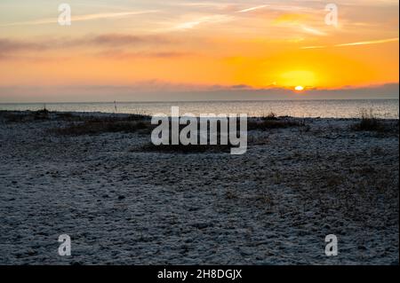 Sole che sorge sul mare con un sottile strato di neve che copre la spiaggia di ghiaia in una mattinata d'inverno sulla costa meridionale del Regno Unito. Foto Stock