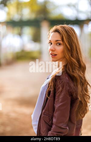 Giovane ragazza naturale che si gira verso la macchina fotografica in abito casual nel parco Foto Stock