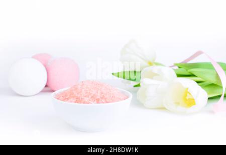 Sale da bagno rosa accanto a bombe saline e tulipani, su sfondo bianco grigio, si riflettono sulla superficie dello specchio del tavolo. Il concetto di cosmetologia Foto Stock