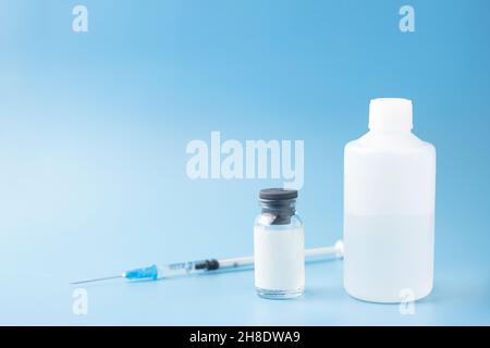 Flacone di vetro per uso medico con spazio di copia, su sfondo blu accanto alla siringa e un flacone di plastica con soluzione salina, medicinale. Messa a fuoco selettiva. Medico Foto Stock
